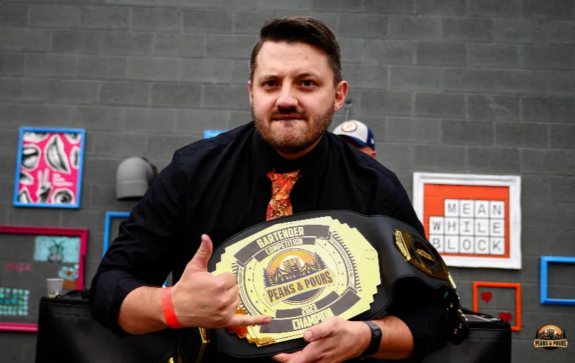 Bartender competition champion holding the Peaks and Pours championship belt at Meanwhile Block in Colorado Springs
