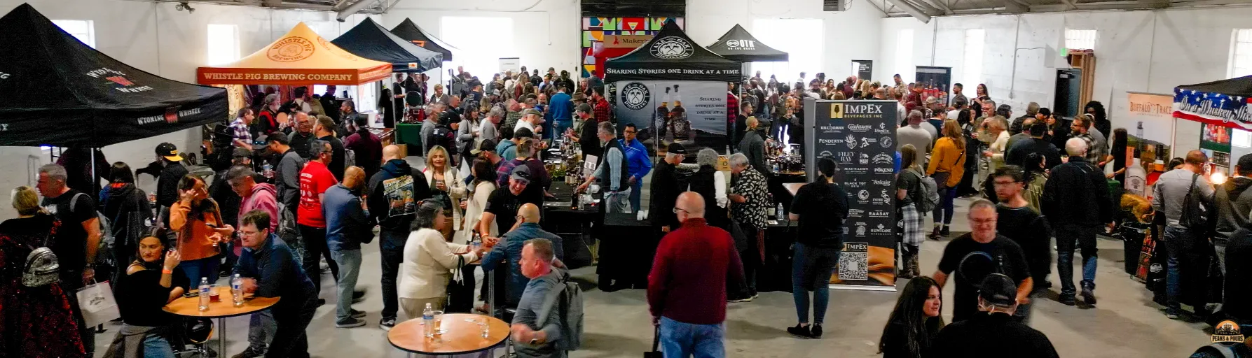 Wide crowd shot of the inaugural Peaks and Pours 2023 event at Meanwhile Block showing packed venue floor with Whistle Pig Brewing and Wyoming Whiskey booths