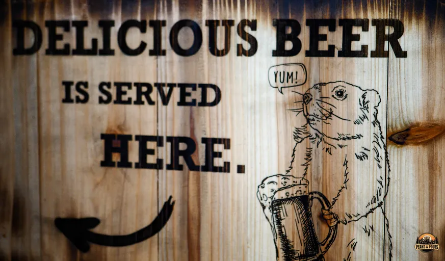 Wooden sign reading Delicious Beer is Served Here with a beaver saying yum at Meanwhile Block