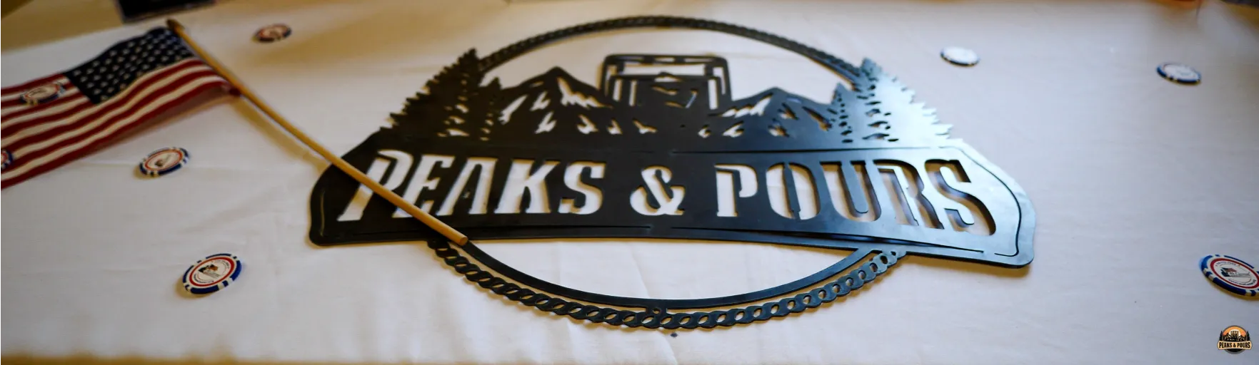 Peaks and Pours metal logo cutout with American flag and branded poker chips on the event registration table